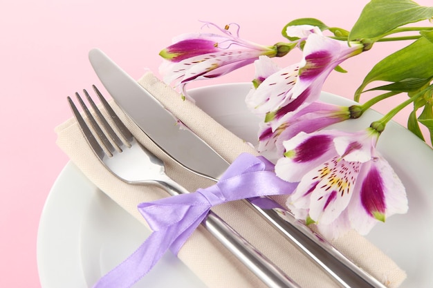 Mesa de comedor festiva con flores sobre fondo rosa