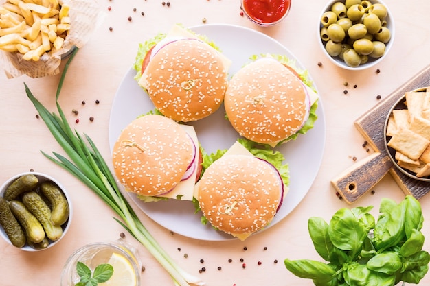 Mesa de comedor con hamburguesas, papas fritas, verduras, salsas, bocadillos y limonada en madera