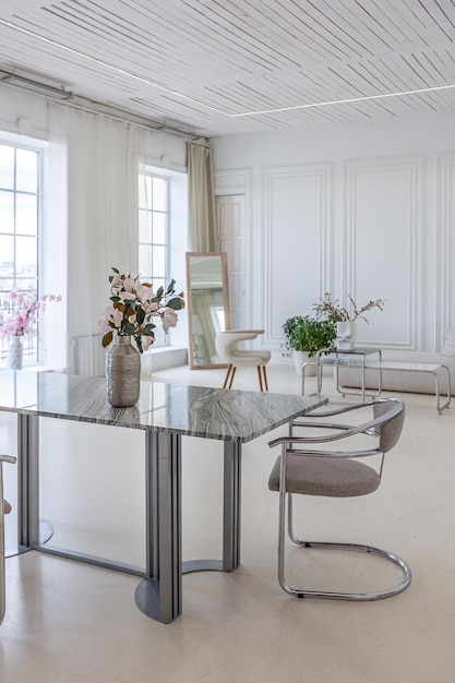 mesa de comedor de mármol y dos sillas con el telón de fondo de una ventana panorámica al interior de un luminoso salón de lujoso estilo barroco con paredes blancas decoradas con estuco antiguo