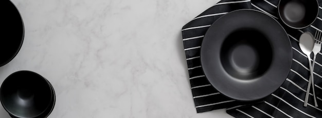 Mesa de comedor de mármol con utensilios de cocina de cerámica negra, cubiertos en servilleta y espacio de copia