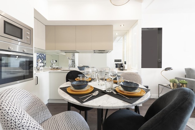 Mesa de comedor redonda de mármol blanco rodeada de sillas tapizadas en un rincón de una cocina tipo loft de planta abierta