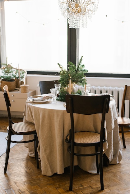 Mesa de comedor con sillas de madera decoradas y servidas para la cena de Navidad al fondo