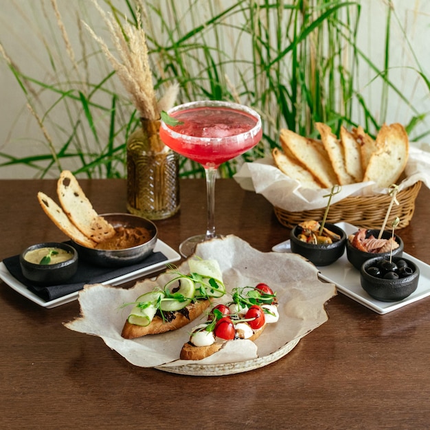 Una mesa con comida y bebida, incluido un cóctel rosa.