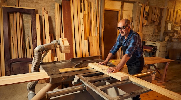 Mesa de corte de madera con sierra circular eléctrica Carpintero profesional senior en tablero de madera de corte uniforme en la fabricación de carpintería de aserradero