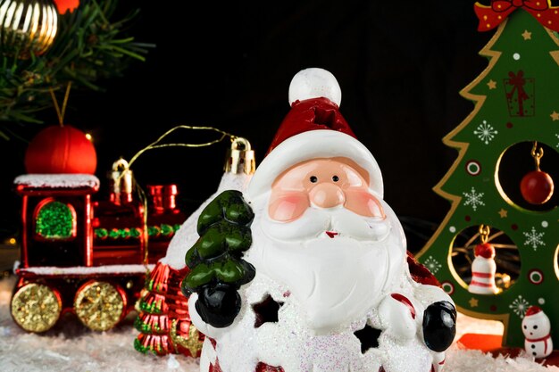 Mesa cubierta de copos de nieve con adornos navideños. Santa Claus, árbol de Navidad con luces y bolas rojas, doradas. Enfoque selectivo.