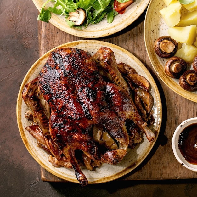 Mesa de ação de graças de férias com pratos clássicos pato vitrificado assado com maçãs batatas cozidas salada verde e molho na mesa de madeira escura com decoração de outono imagem quadrada plana leiga