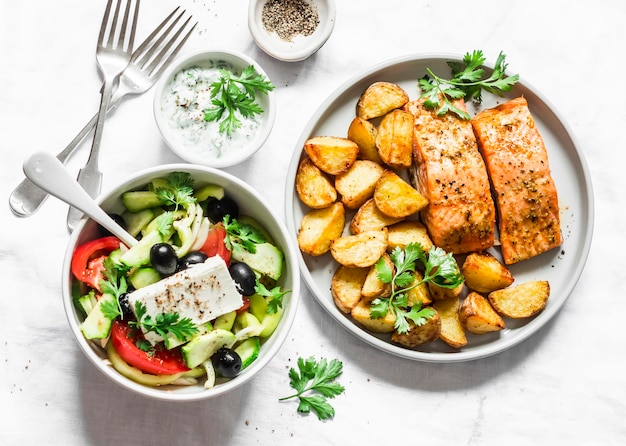 Mesa de almoço mediterrânea salmão de limão assado com batatas salada grega molho tzadziki na vista superior de fundo claro