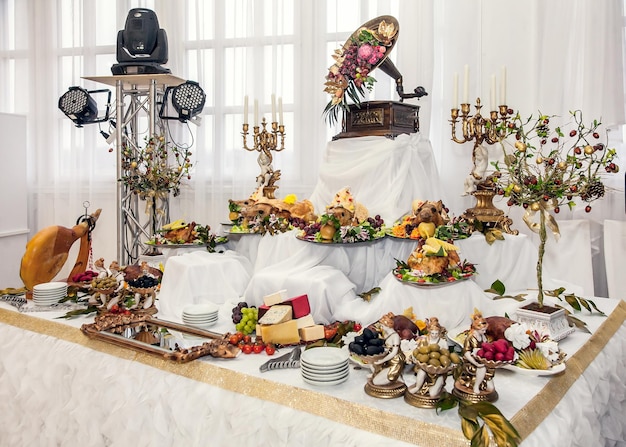 Mesa de buffet com petiscos de carne porcos assados em massa de queijo peru com frutas decoradas com candelabros e gramofone