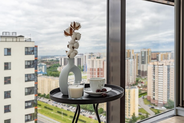 Mesa de café com uma xícara, uma vela, uma cereja e um vaso com um galho de algodão no fundo de