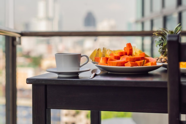 Foto mesa de café da manhã com frutas de café e croisant de pão em uma varanda contra o pano de fundo da cidade grande