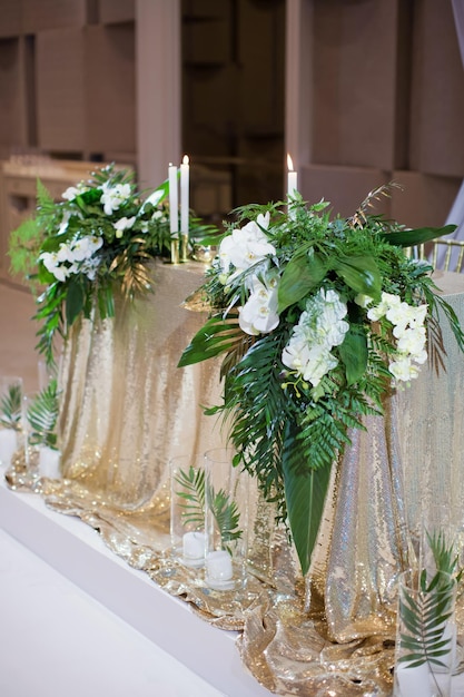 Mesa de casamento com folhas verdes tropicais de decorações douradas e velas acesas em vasos de vidro