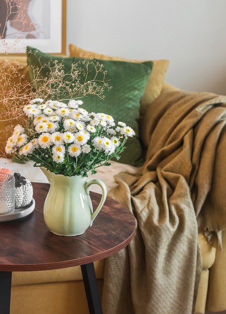 Mesa de centro interior da sala de estar com um buquê de crisântemos poltrona de decoração de outono com almofadas aconchegantes