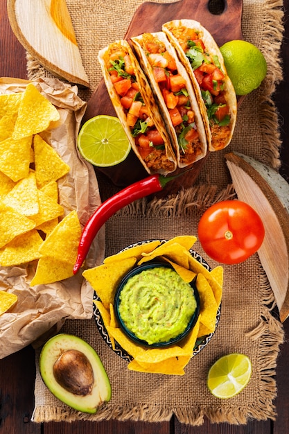 Mesa de comida mexicana com nachos, guacamole, tacos e ingredientes. Tortilha de taco mexicano e nacho em placas de madeira. Comida mexicana hispânica