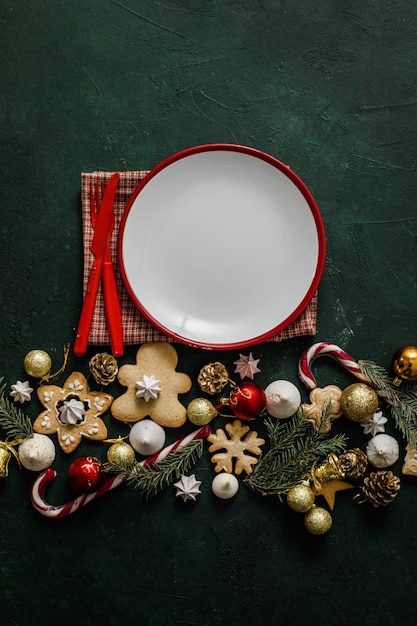 Mesa de configuração de Natal e ano novo. Prato vazio branco com talheres e galhos de árvores de Natal, guardanapo vermelho sobre um fundo vermelho de concreto.