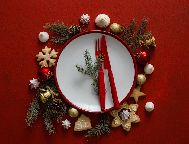 Mesa de configuração de Natal e ano novo. Prato vazio branco com talheres e galhos de árvores de Natal, guardanapo vermelho sobre um fundo vermelho de concreto.