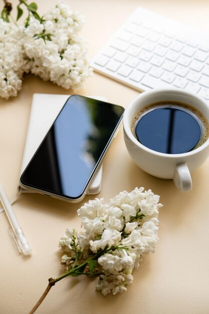 Mesa de cor neutra com teclado flores lilás brancas e smartpohone preto