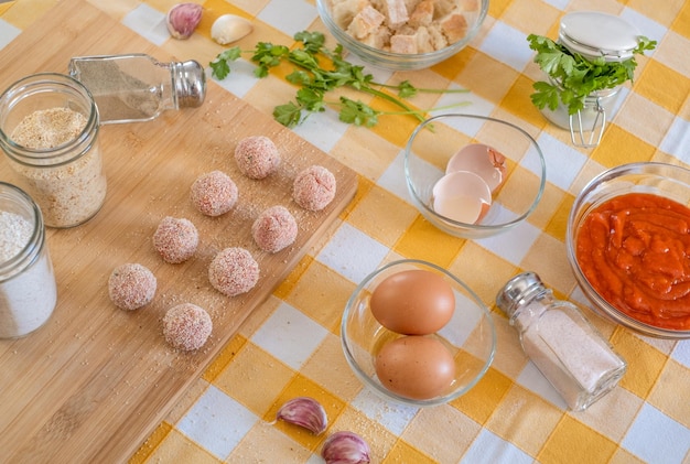 Mesa de cozinha com almôndegas prontas para tábua de madeira e ingredientes crus