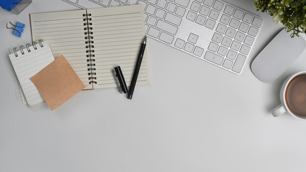 Mesa de escritório branca com bloco de notas, teclado de nota pegajosa e xícara de café Vista superior com espaço para cópia