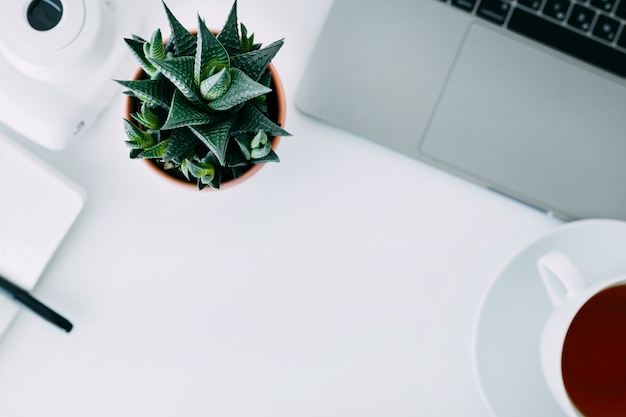 Mesa de escritório branco com laptop, planta de escritório e notebook com caneta, mini câmera e xícara de chá. vista superior com espaço de cópia, lay plana