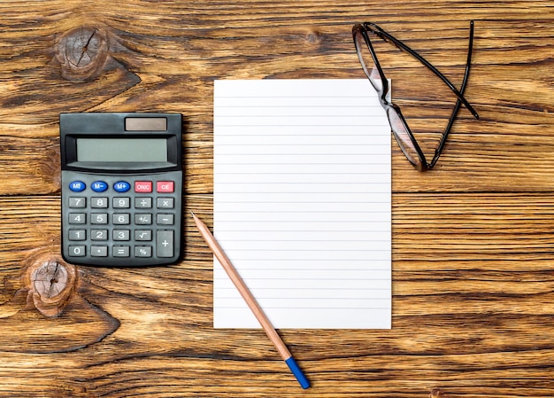 Mesa de escritório com artigos de papelaria Bloco de notas em branco com calculadora e óculos na mesa Vista superior Conceito de negócios