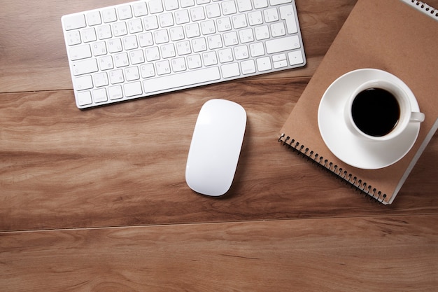 Mesa de escritório com bloco de notas, computador e xícara de café.