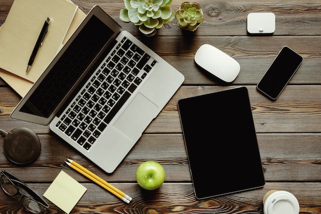 Mesa de escritório com computador portátil, suprimentos e maçã verde, vista superior