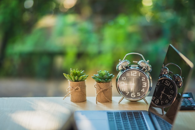 Mesa de escritório com laptop de tela em branco e relógio, planta