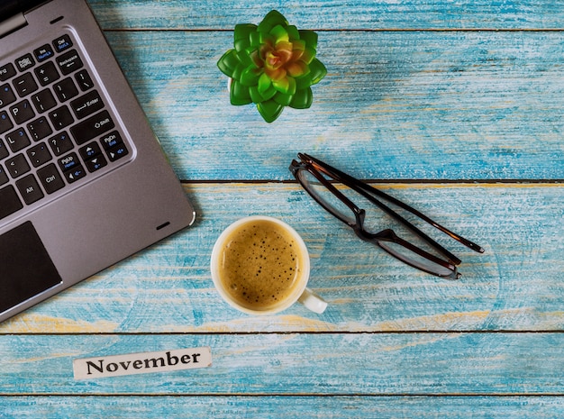 Mesa de escritório com mês de novembro do ano civil, computador e xícara de café, vista de óculos