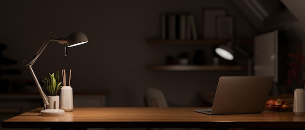 Mesa de escritório de madeira escura moderna à noite sob a luz quente do candeeiro de mesa com laptop