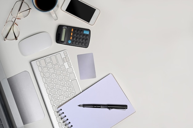 Mesa de escritório de vista superior branca com notebook, calculadora, telefone celular e óculos.