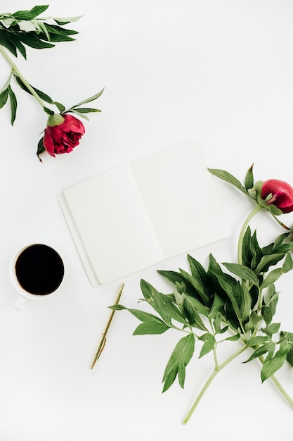 Mesa de escritório em casa mínima com caderno, café e flores de peônia na superfície branca