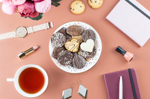 Mesa de escritório em casa plana leigos. Espaço de trabalho feminino com diário, flores, doces, acessórios de moda. Conceito de blogueiro de moda.