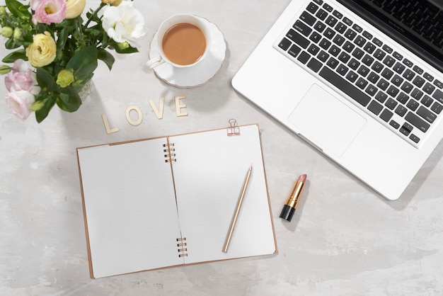 Mesa de escritório em casa plana leigos. Espaço de trabalho feminino com laptop, buquê de lisianthus rosa, batom, diário e carta de AMOR em branco