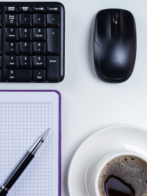 Mesa de escritório. Espaço de trabalho com caderno em branco, teclado, material de escritório e xícara de café em fundo branco.