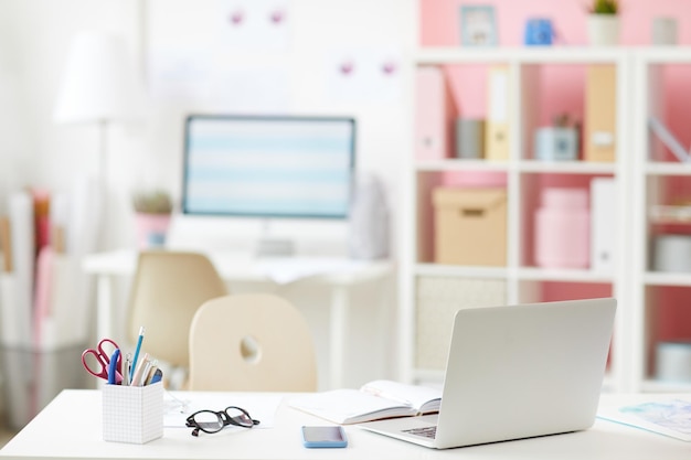 Mesa de escritório moderna com dispositivos e suprimentos em sala aconchegante com prateleiras em segundo plano