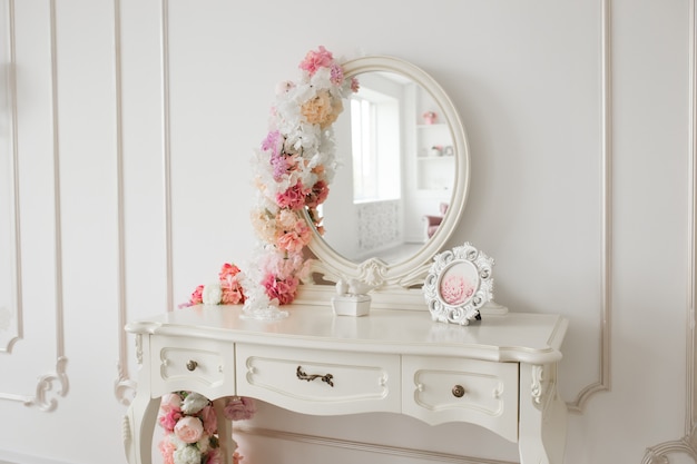 Mesa de estilo vintage com espelho redondo e flores. Quarto branco brilhante.