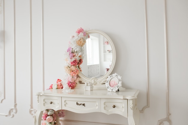 Mesa de estilo vintage com espelho redondo e flores. Quarto branco brilhante.