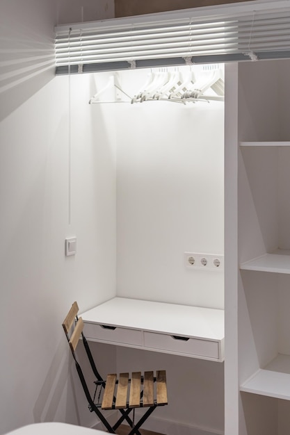 Mesa de estudo branca combinada com guarda-roupa com prateleiras de madeira e cadeira em uma pequena sala de estudantes para