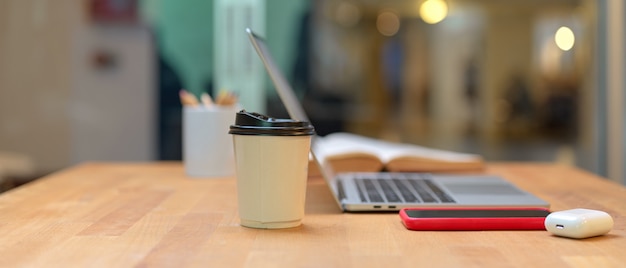 Mesa de estudo com laptop, smartphone, copo de papel, artigos de papelaria e livro aberto na biblioteca