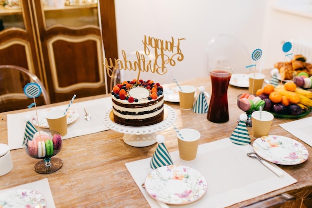 Mesa de férias servida com mesa de bolo de aniversário cheia de pratos vazios de compota de frutas e chapéus de festa Linda mesa posta para festa de aniversário Composição festiva Conceito de celebração