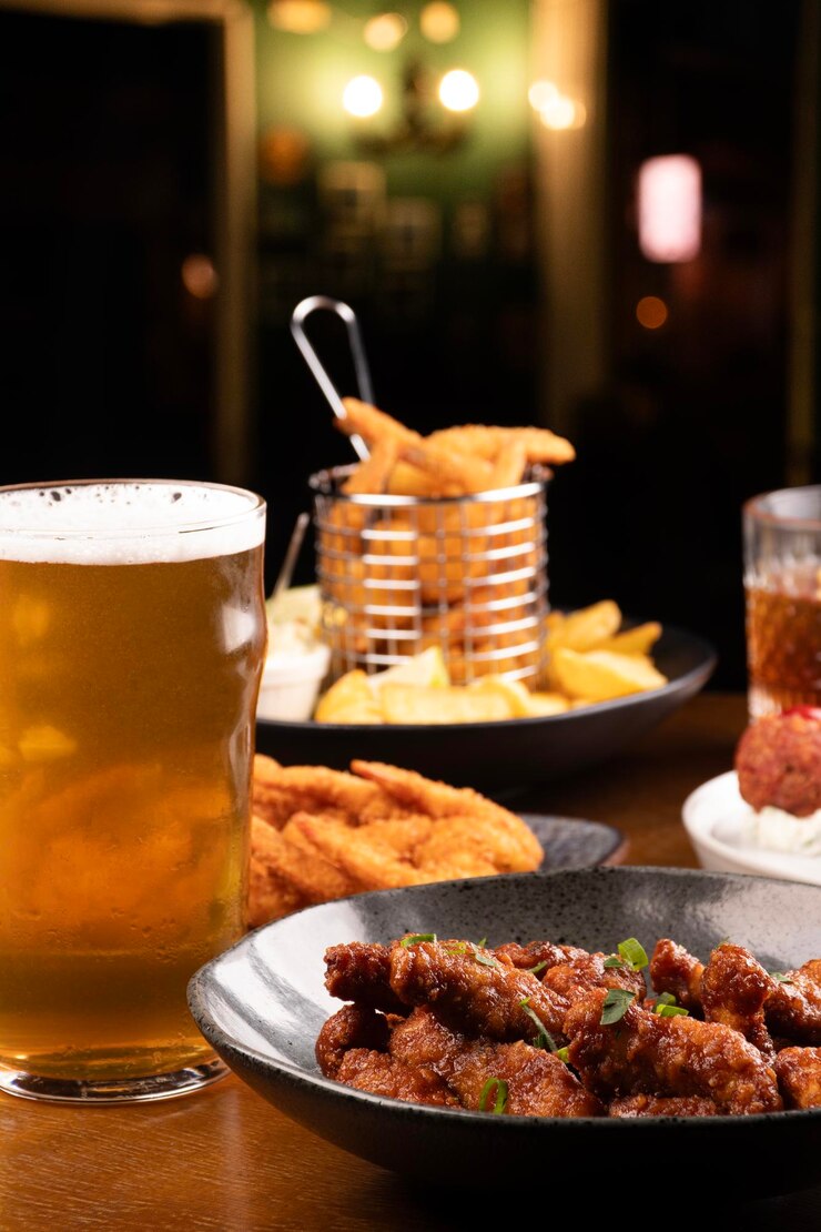Foto mesa de happy hour com cerveja artesanal e bebida e porções variadas de petiscos fritos fundo desfocado com close up de frango teriyaki