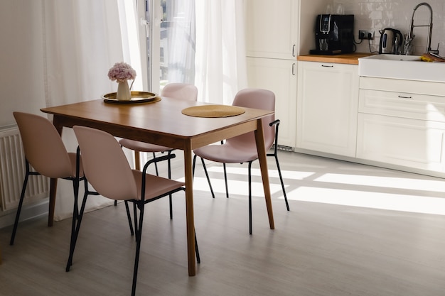 Mesa de jantar de madeira com quatro cadeiras de plástico rosa ao redor e uma flor rosa em uma cozinha de estilo moderno em um dia ensolarado