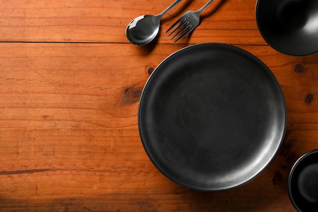 Mesa de jantar de madeira com talheres de cerâmica preto vazio, tigela pequena e espaço de cópia