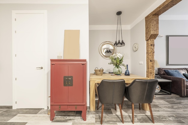 Mesa de jantar em madeira maciça ao lado de um aparador vermelho estilo asiático em uma sala com pilares de madeira maciça