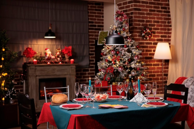 Mesa de jantar servida de Natal, preparação de jantar festivo em família, lindo lugar decorado. Copos de vinho, pratos, velas, talheres na tradicional toalha de mesa vermelha e verde