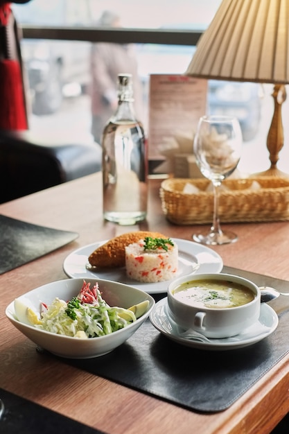 Foto mesa de jantar: um prato de sopa, risoto com costeleta e salada de legumes vista lateral