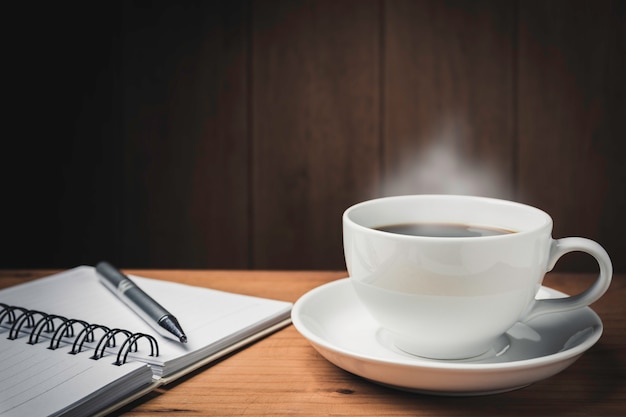 Mesa de madeira com café. espaço de trabalho com copo de caderno, caneta e café no espaço de madeira com espaço de cópia.