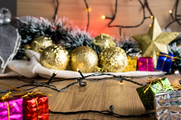 Mesa de madeira com enfeites de Natal. Bolas vermelhas, prata e ouro, caixas de presente, luzes, panetone, árvore de natal e outros. Foco seletivo.