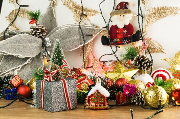 Mesa de madeira com enfeites de Natal. Bolas vermelhas, prata e ouro, caixas de presente, luzes, Papai Noel, Panetone, Árvore de Natal e outros. Foco seletivo.