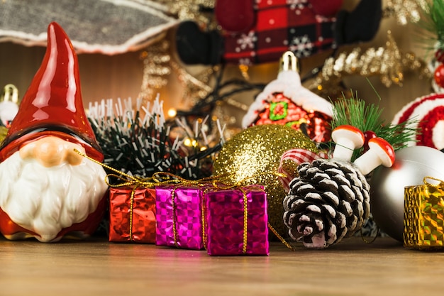 Mesa de madeira com enfeites de Natal. Bolas vermelhas, prata e ouro, caixas de presente, luzes, Papai Noel, Panetone, Árvore de Natal e outros. Foco seletivo.